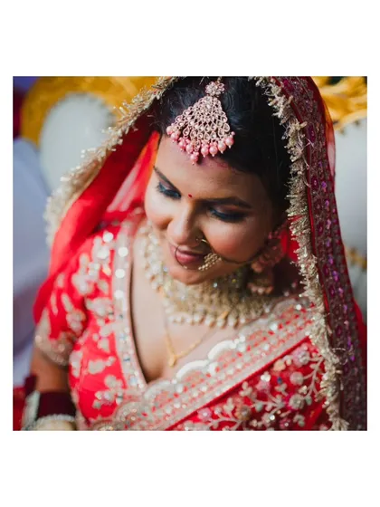 A demure, downward glance from the bride, showcasing her intricate makeup and the delicate details of her maang tikka.