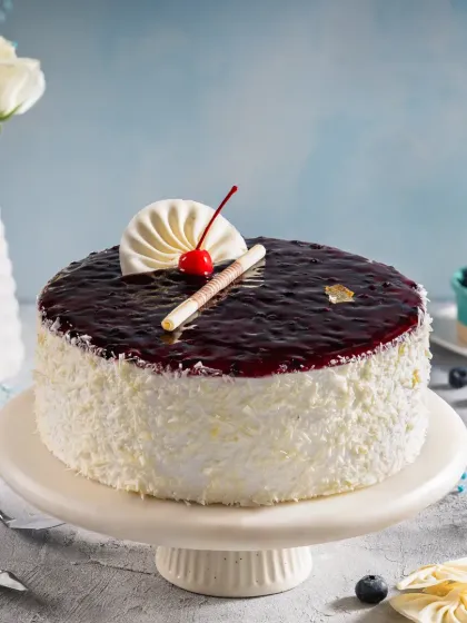 A blueberry cheesecake with a glossy fruit topping and white chocolate shavings, styled with fresh blueberries to enhance its appeal for online catalogs.