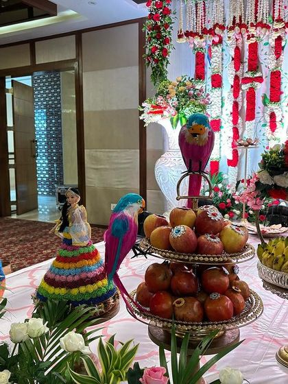 A close-up of the offering table with colorful parrot props and traditionally dressed dolls.