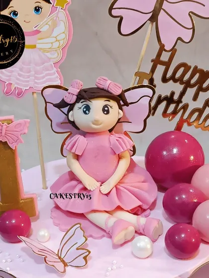 A close-up of the fondant girl and butterfly decorations on this two-tier pineapple cake. The pink theme and delicate details make it perfect for a first birthday celebration.