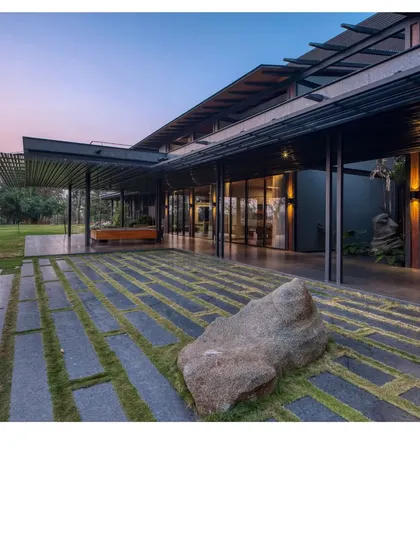 The Lakeshore house at dusk, a filter for breezes and views on Lake Osman Sagar. Here, a prefabricated steel skeleton and walls of rammed earth from the site itself come together, creating a home that almost disappears into the treeline.
