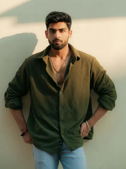 A model in an olive green shirt poses against a sunlit wall. This shot demonstrates our use of natural light and shadow to create warm, compelling portraits.