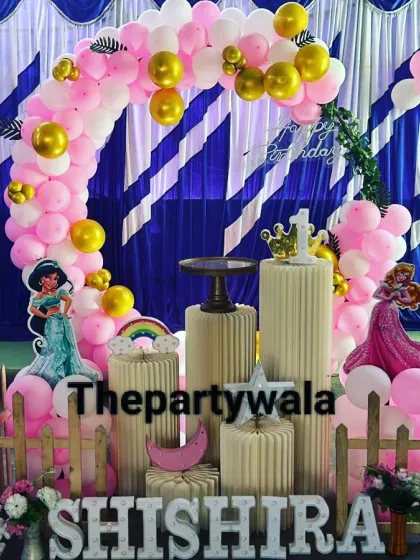 This princess theme uses a blue and white striped backdrop for a unique look. The pink and gold balloon arch with princess cutouts stands out beautifully against it.