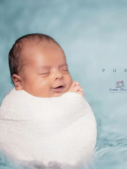 This is a classic 'potato sack' swaddle pose, which babies often find very comforting. The simple wrap and soft blue backdrop draw all the attention to the baby's sweet, sleepy smile.