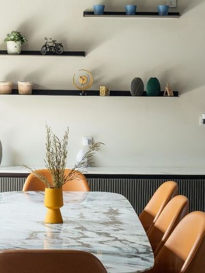 A closer look at the dining space, where we paired contemporary orange chairs with a minimalist table. The floating shelves are styled with simple decor, keeping the focus on clean lines and uncluttered living.