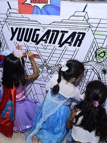 A group of kids, including the birthday boy in his Spider-Man costume, collaborate on a giant coloring wall. This is a fantastic activity for group creativity.