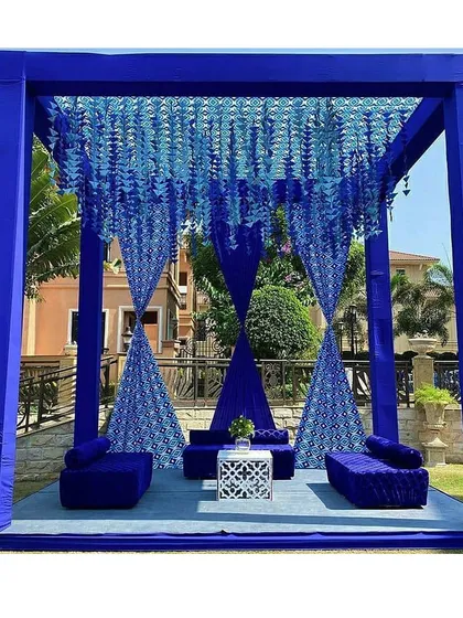 A stunning seating area designed for a Blue Pottery themed event. The deep blue drapes, floral hangings, and plush velvet seating created a luxurious and unique ambiance.