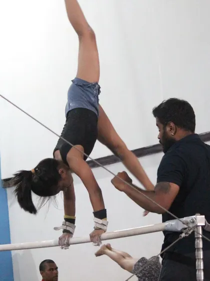 A coach provides hands-on support during uneven bar training. This is crucial for helping gymnasts learn advanced skills like handstands on the bar.