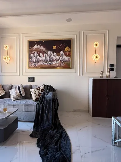 This living room design uses classic wall molding, elegant sconce lighting, and a comfortable L-shaped sofa to create a sophisticated and timeless feel. The large artwork of seven horses adds a dynamic focal point.