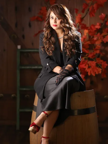 A sophisticated studio portrait of Megha Sharma. The warm tones of the background and her elegant pose create a rich, classic look.