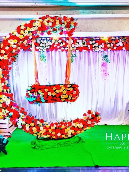 This vibrant crescent moon cradle is decorated with bright red and yellow flowers. The setup is placed against a white curtain backdrop, making the colors pop.