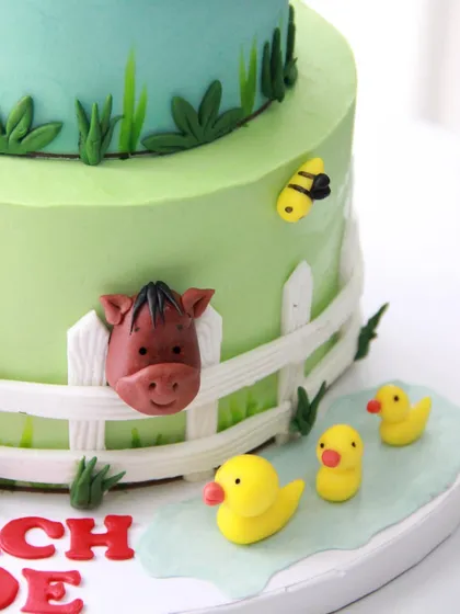 A detail of the lower tier of the farm cake, with a horse peeking over the fence and little ducklings going for a swim.