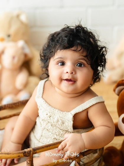 A classic baby portrait with a soft, neutral background and teddy bear props.