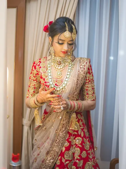 A bride adjusts her jewelry in a moment of quiet preparation. This full-length shot captures the elegance of her red lehenga and the final touches before the ceremony.