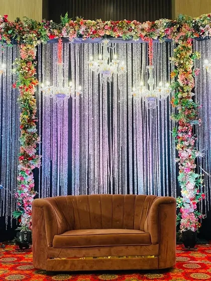 For this reception, I created a glamorous photo point with a backdrop of shimmering silver strings and elegant chandeliers. The floral borders and plush brown sofa complete this luxurious and sparkling setup.