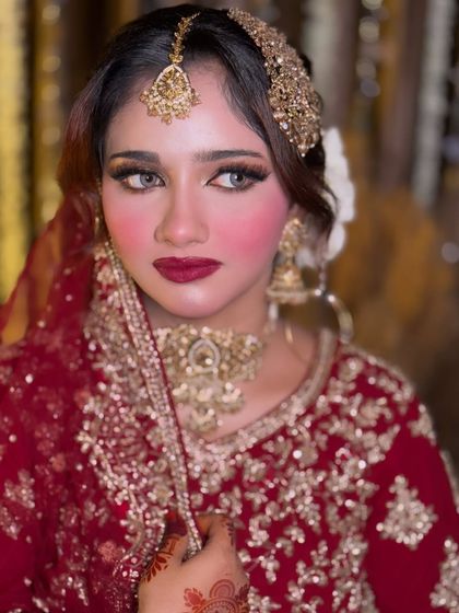 A close-up portrait of a bride with a bold red lip and glowing skin. This look is a perfect example of classic Nikkah makeup that highlights the bride's features beautifully.