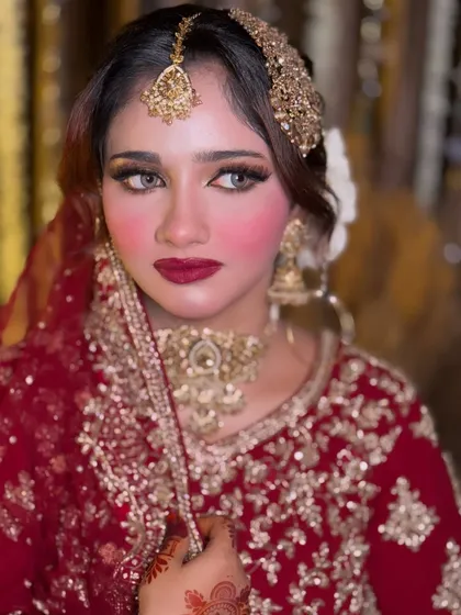 A close-up portrait of a bride with a bold red lip and glowing skin. This look is a perfect example of classic Nikkah makeup that highlights the bride's features beautifully.