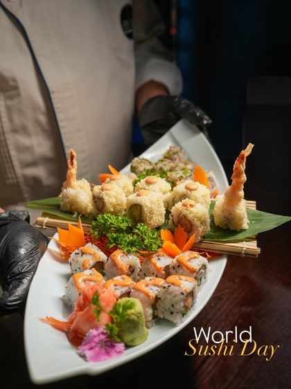 A chef presents a boat-shaped platter of assorted sushi rolls, including our popular Ebi Tempura and salmon rolls. This presentation is perfect for sharing at the table.