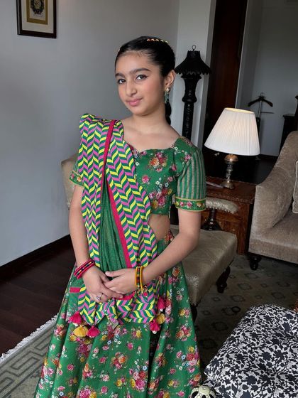 A young client looking adorable in her green lehenga with a colorful braided hairstyle. This is a perfect example of a festive hairstyle for kids.