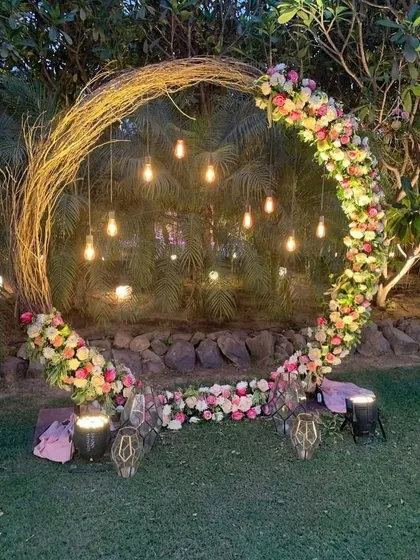 This rustic twig arch, decorated with fresh flowers and hanging Edison bulbs, creates a magical photo point for an evening Mehndi or Haldi function. It's a beautiful blend of natural and modern elements.