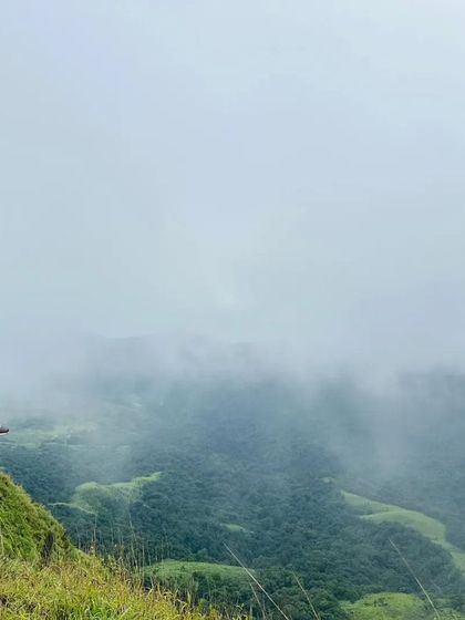 A trekker sitting on a cliff edge, enjoying the misty view from Gangadikal peak.