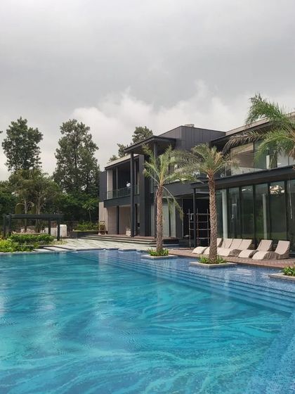 A wide shot of a nearly complete farmhouse pool, showcasing its generous size and the beautiful blue mosaic tiles. The surrounding deck and lounge chairs signal a space designed for ultimate relaxation and entertainment.