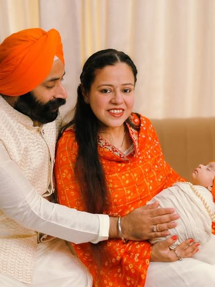 The first family portrait as three. This image captures the parents' joy and wonder as they hold their newborn, dressed in beautiful orange and white traditional clothing.