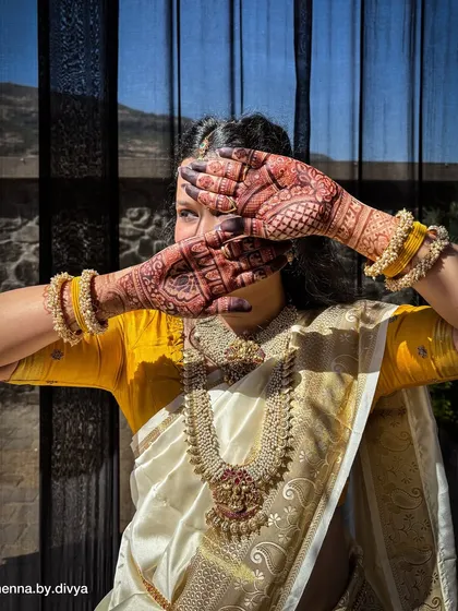 Another artistic shot of the bride, with her henna-stained hands partially covering her face. The sunlight highlights the rich, deep color of the mehendi.