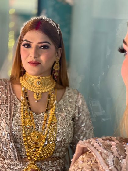 A reception look featuring heavy gold jewelry. The makeup is kept elegant and balanced, with a focus on flawless skin and defined eyes.
