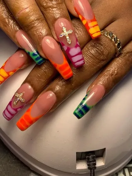 A very long and colorful set of nails with rainbow-colored tips and sparkling cross charms.
