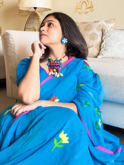 A thoughtful pose in the blue mul cotton saree. The colorful fabric jewelry adds a playful, bohemian touch to the look.