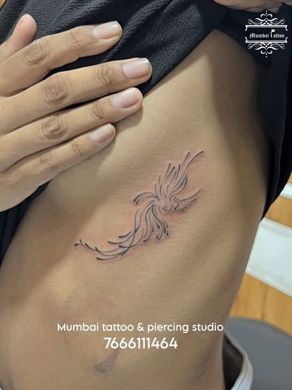 A fine line phoenix tattoo on the ribcage, symbolizing rebirth and resilience. The minimalist style makes this powerful symbol feel light and elegant, a popular choice for a discreet but meaningful tattoo.