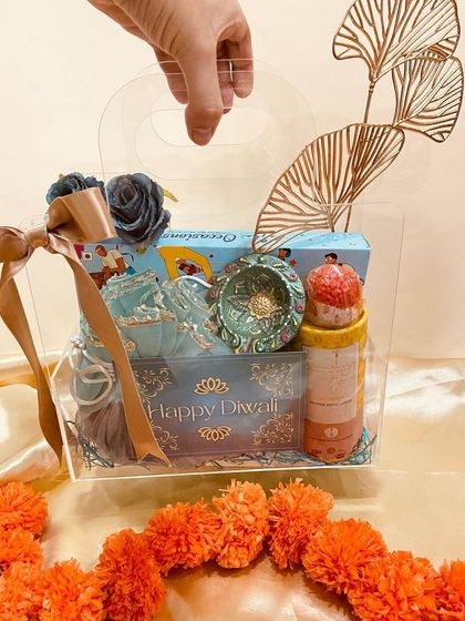 A modern transparent acrylic box hamper for Diwali. This gift includes a decorative ashtray, candles, and other festive items, all beautifully arranged and visible.
