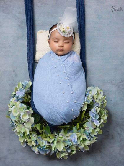 A little angel in blue, adorned with a delicate headband and pearls. This hanging wreath prop, decorated with hydrangeas, creates a dreamy and ethereal feel.