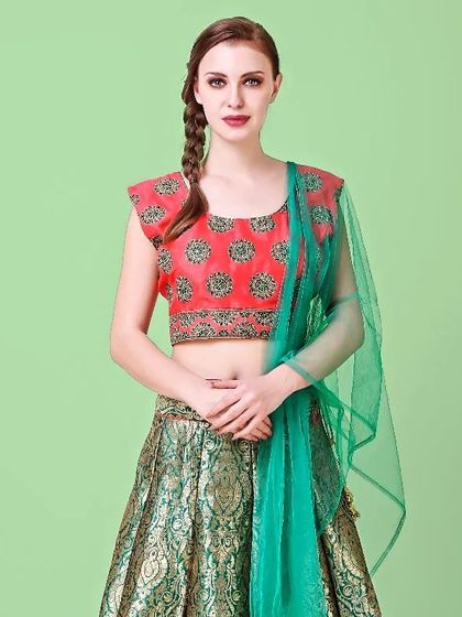 An international model wearing a brocade lehenga with a contrasting red and green blouse and dupatta, shot against a solid color background.