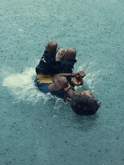The pure, uninhibited joy of the monsoon. A young boy splashes playfully in a large puddle, a perfect example of the candid, energetic moments that the rainy season brings to the city's streets.