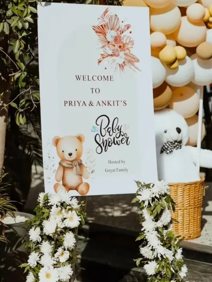 A personalized welcome sign for Priya and Ankit's baby shower, featuring a cute teddy bear graphic and elegant floral details.