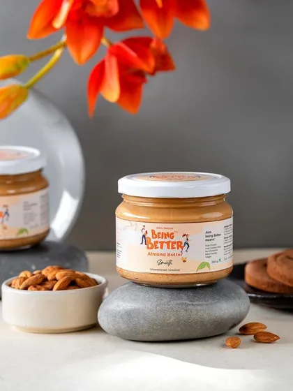 An elegant and calm product shot for Being Better's almond butter. The use of stones and a single flower creates a serene, spa-like feel, associating the product with wellness and self-care.