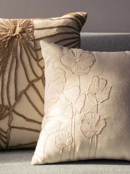 A pair of our nature-inspired embroidered cushions. The one on the right features a bold, graphic pattern, while the one on the left showcases a more delicate, linear floral design, demonstrating the range of our embroidery techniques.