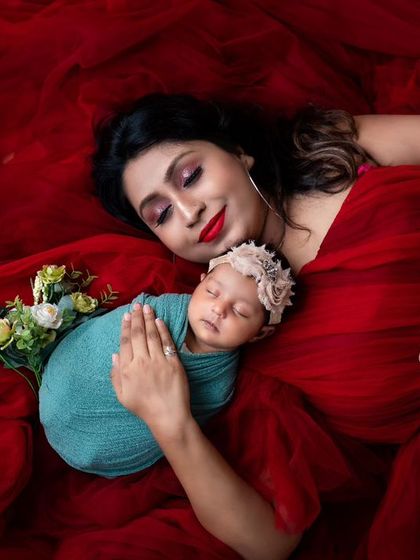 A mother in a flowing red gown lies with her newborn. This dramatic and artistic pose creates a stunning visual, combining motherhood with high-fashion portraiture.