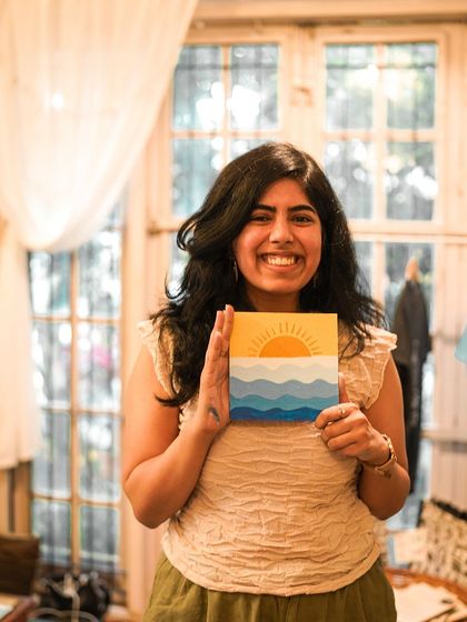 A participant proudly displays her beautiful sunset painting from the art with kittens workshop.