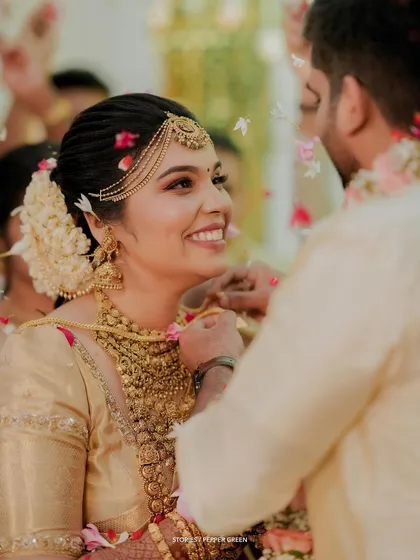 The sacred thali tying moment, the bride's happy smile captured as flower petals rain down.