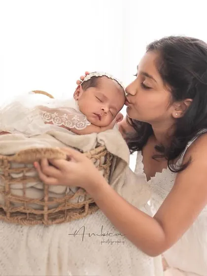 A soft kiss for the new baby. The older sister leans over the basket to give her sibling a gentle peck on the forehead, a truly precious moment.