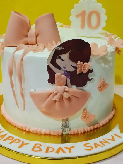 A sweet and delicate ballerina-themed cake for a 10th birthday. The design includes a large fondant bow and a graceful dancer illustration.