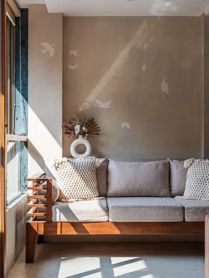 Sunlight streaming into the clinic's seating area. The combination of a simple wooden sofa frame, comfortable cushions, and subtle bird decals on the wall creates a peaceful and cozy corner for clients.