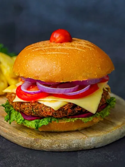 A straight-on shot of a classic burger, highlighting its height and all the fresh ingredients. The dark background ensures the burger is the undisputed hero of the image.