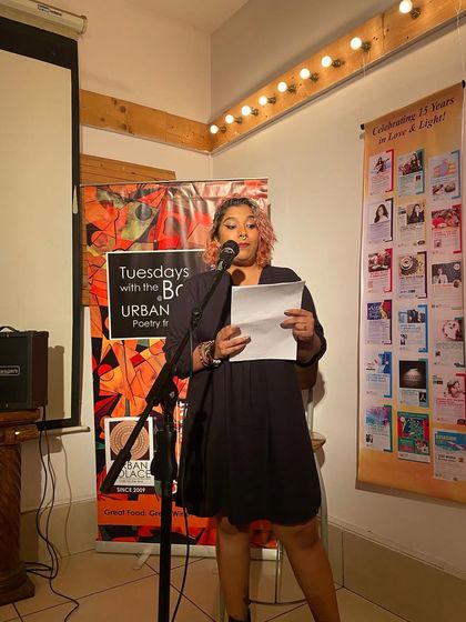 A performer reads from a sheet of paper, her words filling the room. Our open mic is a platform for both seasoned poets and first-time speakers.