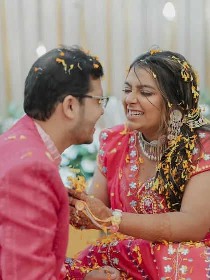 A bride and groom share a laugh while being covered in flower petals during their Haldi. We focus on the couple's interaction and shared joy.