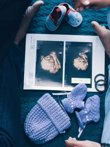 A story told from above. This flat-lay style shot includes the ultrasound photos, tiny shoes, and the couple holding hands. It's a creative and intimate way to announce their journey into parenthood.