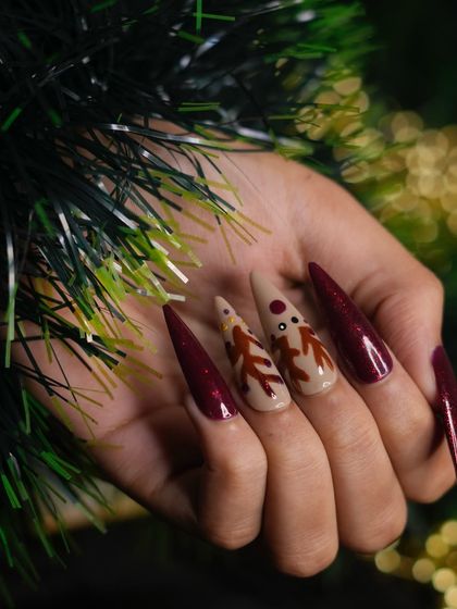 Another perspective of the reindeer nail set, showcasing the length and dramatic shape of the stiletto extensions against a festive green background.